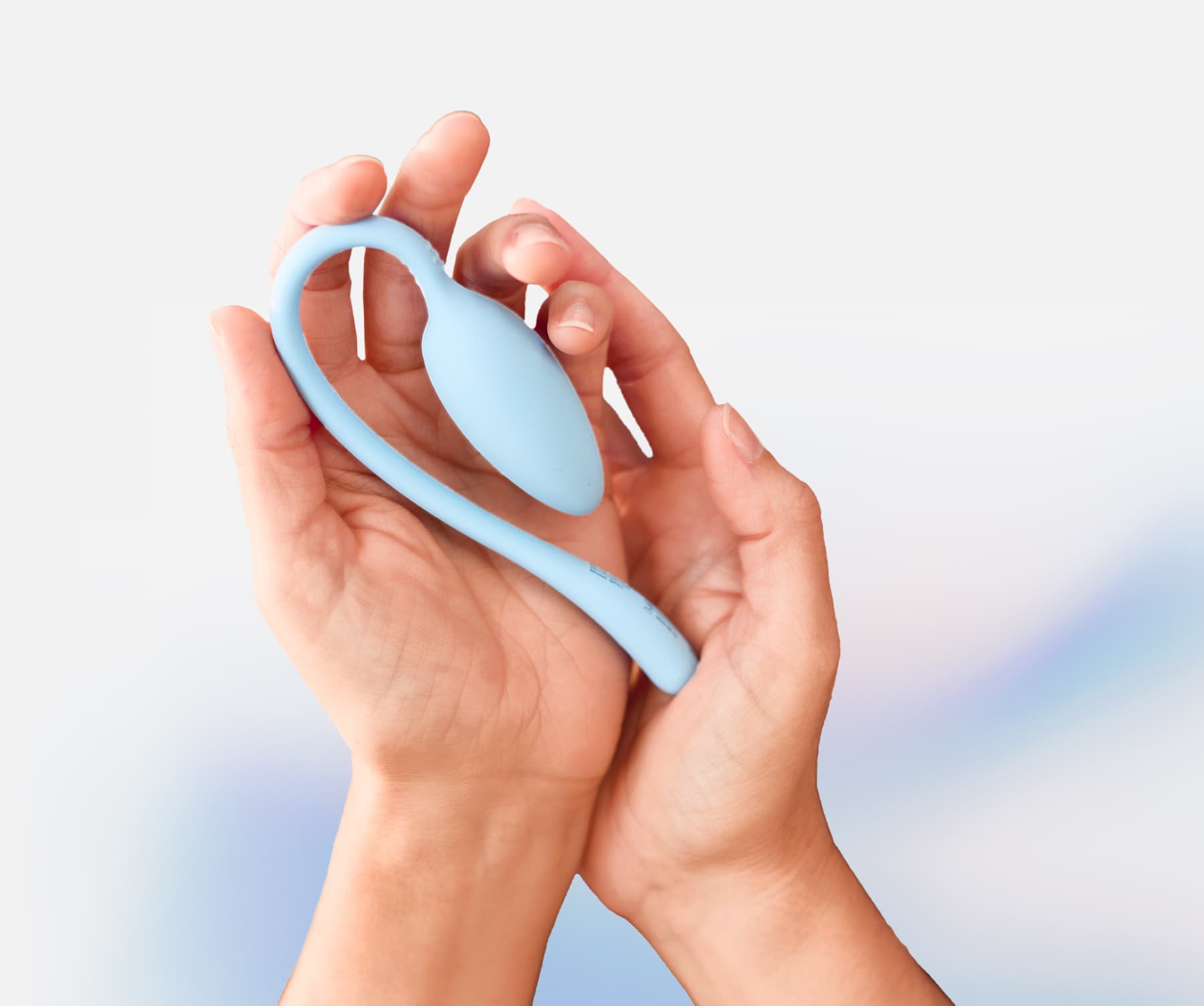 Hands holding a light blue, oval-shaped personal wellness device with a flexible tail against a soft gradient background.