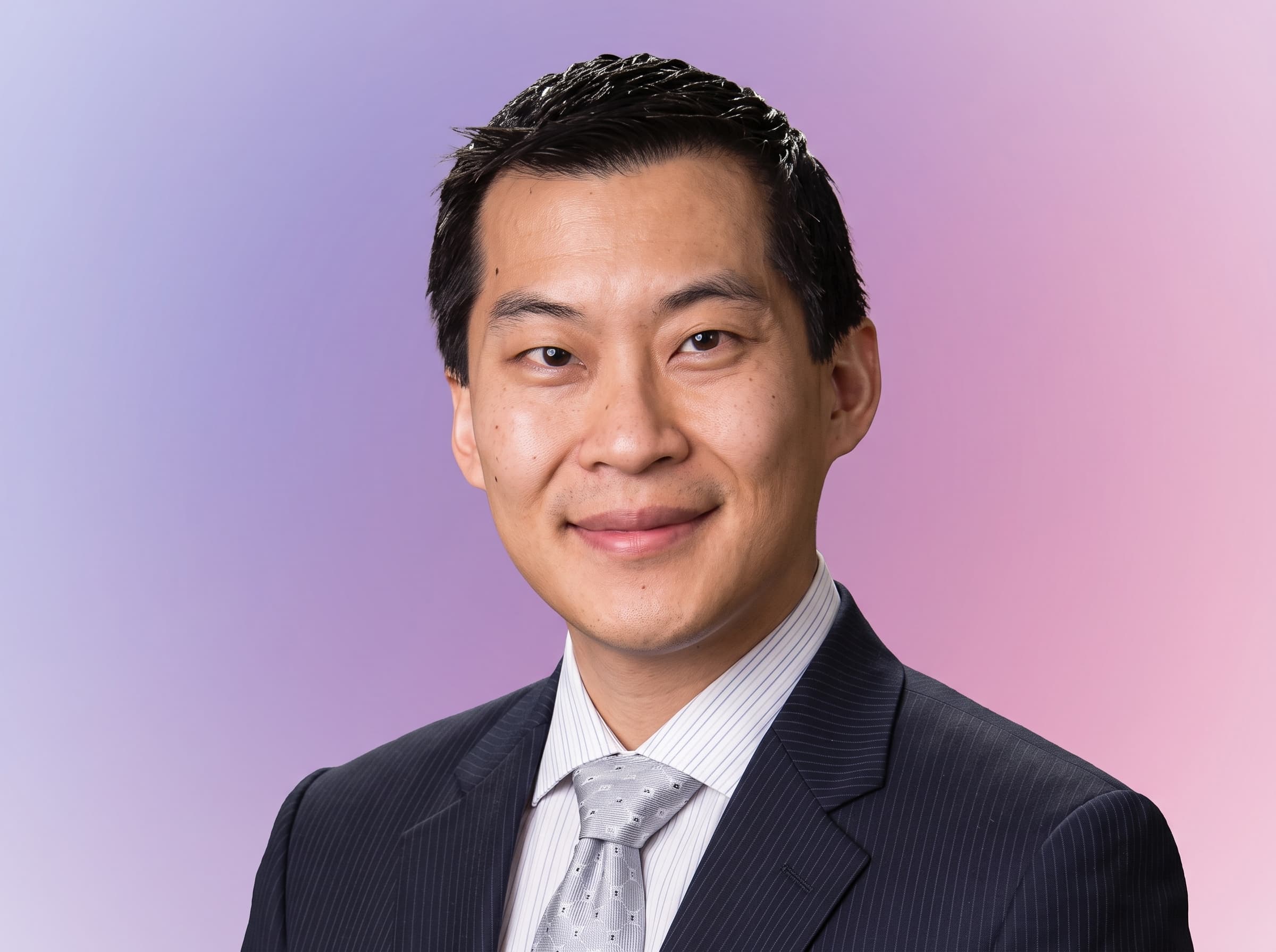 A man in a suit and tie smiles at the camera against a gradient background.