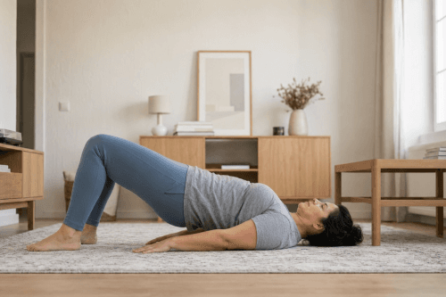 Woman practicing a bridge pose on a rug in a living room with wooden furniture and soft lighting.